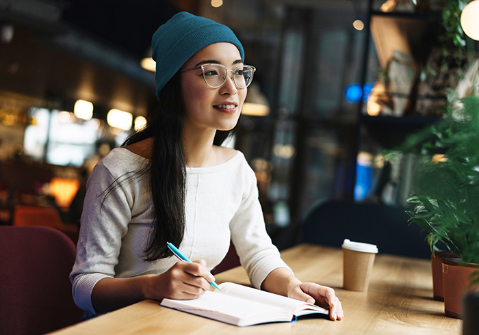 A girl student wearing a cap and specs writing something on her notepad